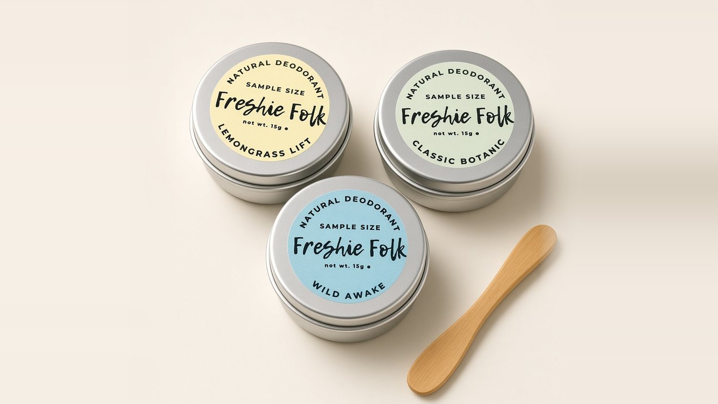 Three small sample-size Freshie Folk deodorant balms, Lemongrass Lift, Classic Botanic and Wild Awake, beside a bamboo applicator on a soft cream background.